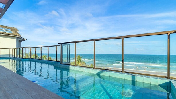 A clear view of a swimming pool with a glass barrier, overlooking a beach and ocean. - Cupe Suites #118 Beachfront by Carpediem (Ipojuca)
