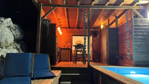 An outdoor wooden deck with a pool, a covered seating area with cushions, and a view of the interior.