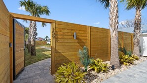 A wooden fence with a gate, palm trees, and a paved walkway. - Small Serenity 1•Fully Remodeled•Beach Gear•Bikes• (Miramar Beach)