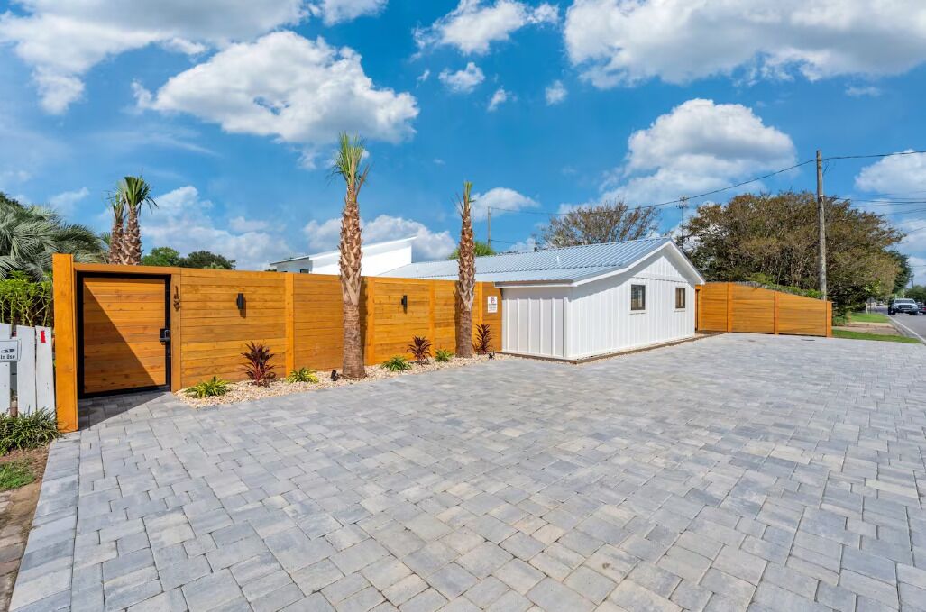 Un bâtiment moderne avec une clôture en bois, une allée pavée et une petite construction blanche.