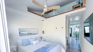 Quarto com uma cama, um ventilador de teto, um quadro e vista para um corredor.