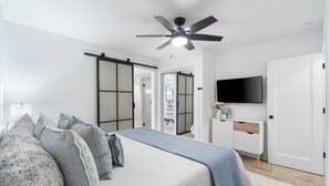 A bedroom with a bed, a dresser, a television, and a sliding door closet. - Small Serenity 4•Fully Remodeled•Beach Gear•Bikes (Miramar Beach)