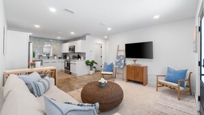 A modern living room with a sofa, coffee table, and a TV mounted on the wall. - Small Serenity 4•Fully Remodeled•Beach Gear•Bikes (Miramar Beach)