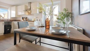 A modern kitchen with white cabinets, a wooden dining table, and two potted plants. - 3 Bedroom with Parking, Close to Town Centre (Redcar and Cleveland)