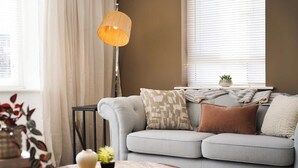 A modern living room with a grey sofa, patterned cushions, a small table with a vase and plant, and a hanging lamp. - 3 Bedroom with Parking, Close to Town Centre (Redcar and Cleveland)