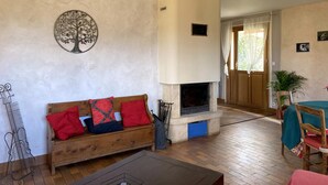 A living room with a wooden sofa, a fireplace, and a dining area with a table and chairs. - Large chalet, parking, pets welcome - 11 guests near Vichy (Le Vernet)