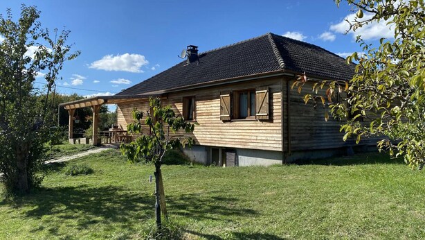 A wooden house with a tiled roof, a covered porch, and a small tree in the front yard. - Large chalet, parking, pets welcome - 11 guests near Vichy (Le Vernet)