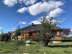 Une maison en bois avec un toit en tuiles, un petit porche et un arbre devant.