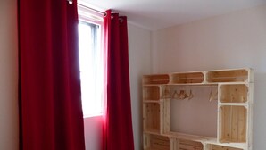 A bedroom with a bed, red curtains, and a wooden wardrobe with multiple compartments. - Modern apartment with country view - 2 guests (Le Vernet)