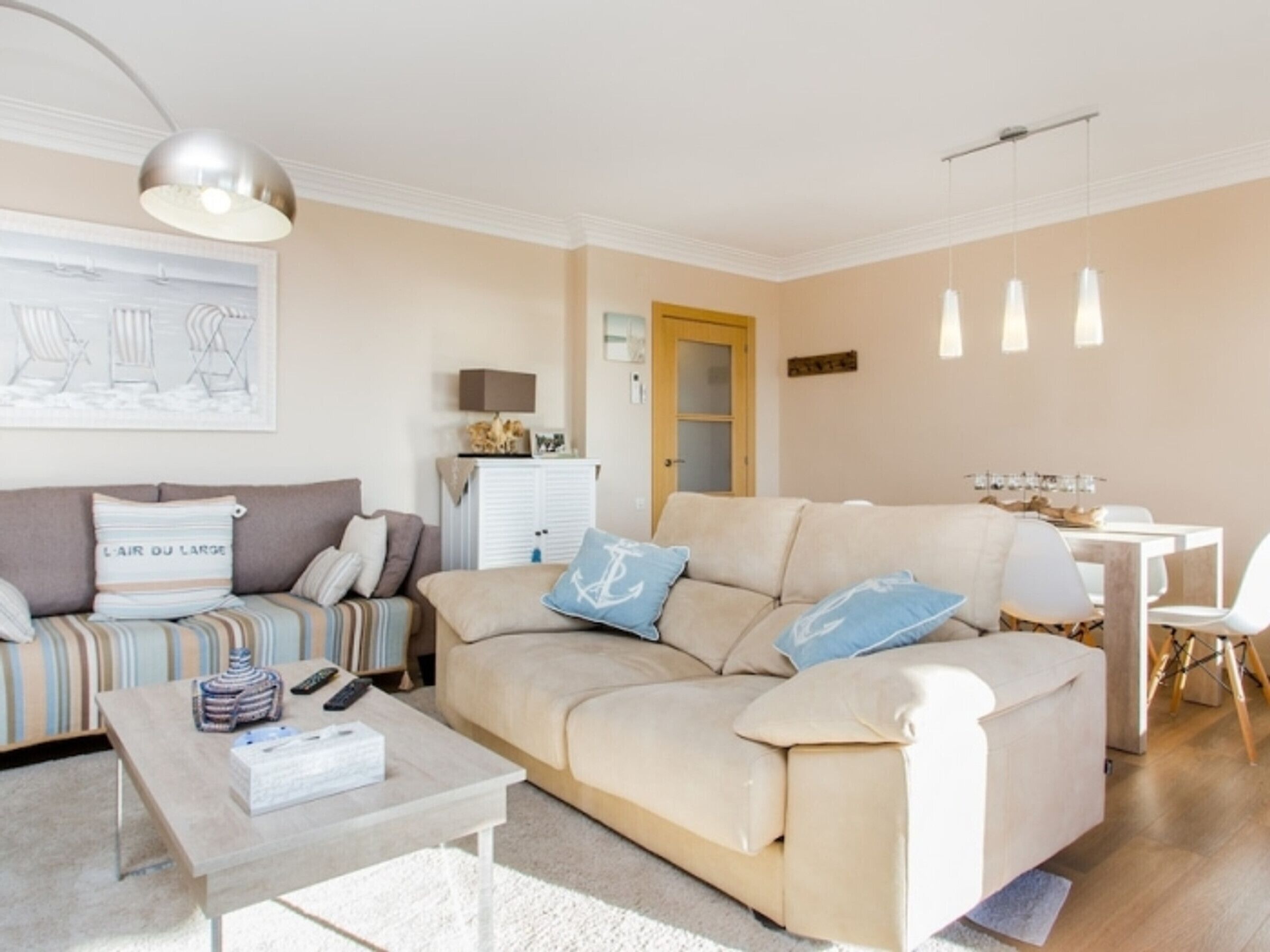 Een woonkamer met een beige bank, een salontafel, en een eetgedeelte met een witte tafel en stoelen.