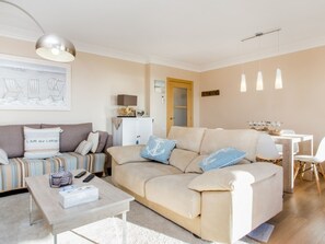 Ein Wohnzimmer mit einem beigefarbenen Sofa, einem Couchtisch und einem Essbereich mit weißem Tisch und Stühlen.