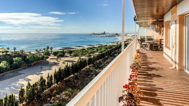 A balcony with a view of the sea and beach, a wooden deck, and potted plants. - Bright apartment with terrace and parking near the beach (Tarragona)