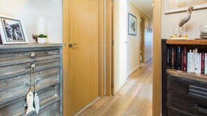A hallway with wooden flooring, a wooden door, a bookshelf with books, and a framed picture on the wall. - Bright apartment with terrace and parking near the beach (Tarragona)