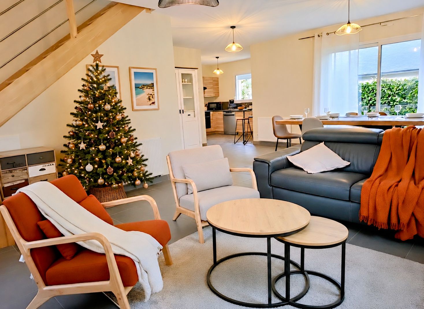 Un salon moderne avec un sapin de Noël, des sièges et une vue sur la cuisine et la salle à manger.