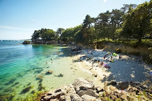 A beach with clear turquoise water, rocky shore, and dense trees. - Cozy house with a quiet, fenced-in yard—3 km from the beach (Fouesnant)