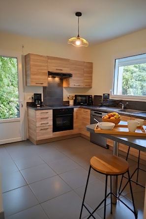 Une cuisine moderne avec des meubles en bois, un four noir, un four à micro-ondes et un coin repas comprenant une table et des tabourets en bois.