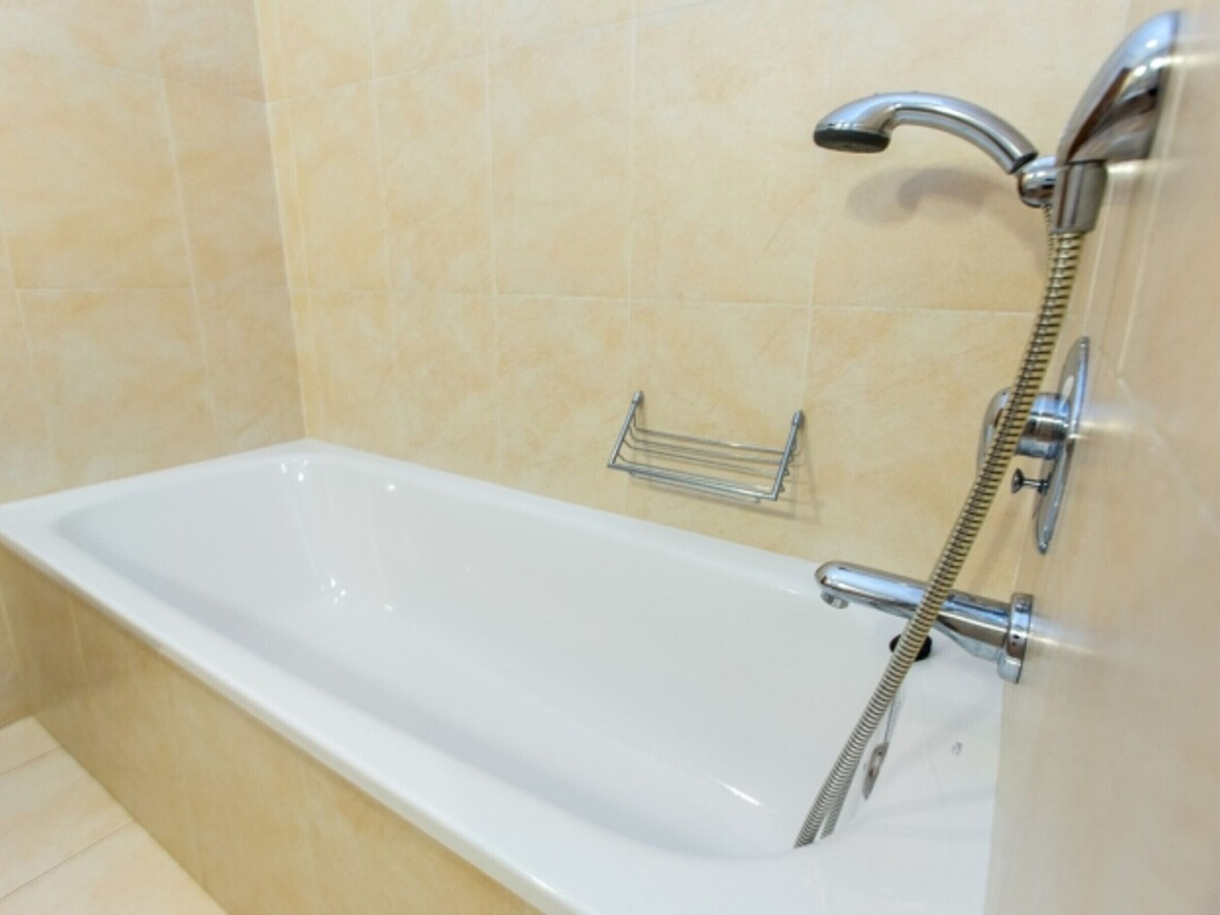 Una bañera blanca con un cabezal de ducha manual y un perchero para toallas.