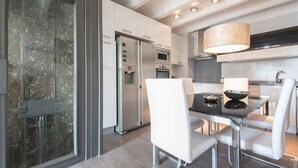 Een moderne keuken met een eetgedeelte, met een glazen deur, roestvrijstalen apparatuur en modern wit meubilair.