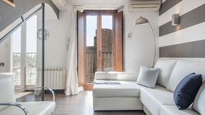 Een moderne woonkamer met een witte bank, een glazen deur die uitkomt op een balkon en een groot raam.