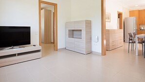 Ein modernes Wohnzimmer mit Flachbildfernseher, einer eingebauten Unterhaltungseinheit und einer Küchenzeile mit Holzschränken und einem Kühlschrank.