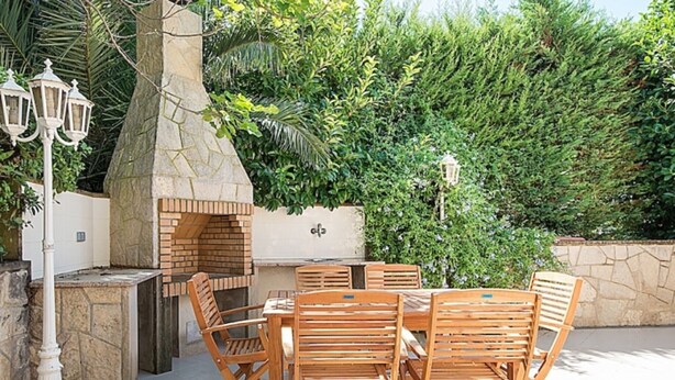 Eine Terrasse im Freien mit Kamin aus Stein, Holzsesseln und Tischen.