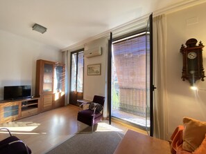 Ein Wohnzimmer mit Fernseher, einem Holzschrank, einem violetten Sessel und einem Balkon mit Blick.