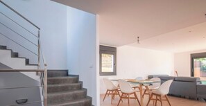 Ein modernes Interieur mit einer Treppe, einer Essecke mit Stühlen und einem Tisch sowie einem grauen Sofa.