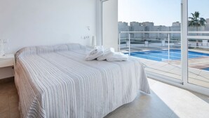 Et moderne hotelværelse med en stor seng, et sengebord og udsigt til en swimmingpool gennem en glasdør.