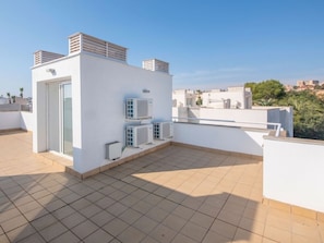 Eine Dachterrasse mit weißer Fassade, Klimaanlagen und freiem Blick auf die Stadtlandschaft.