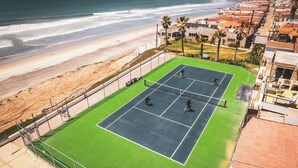 Uma quadra de tênis com vista para a praia e o oceano.