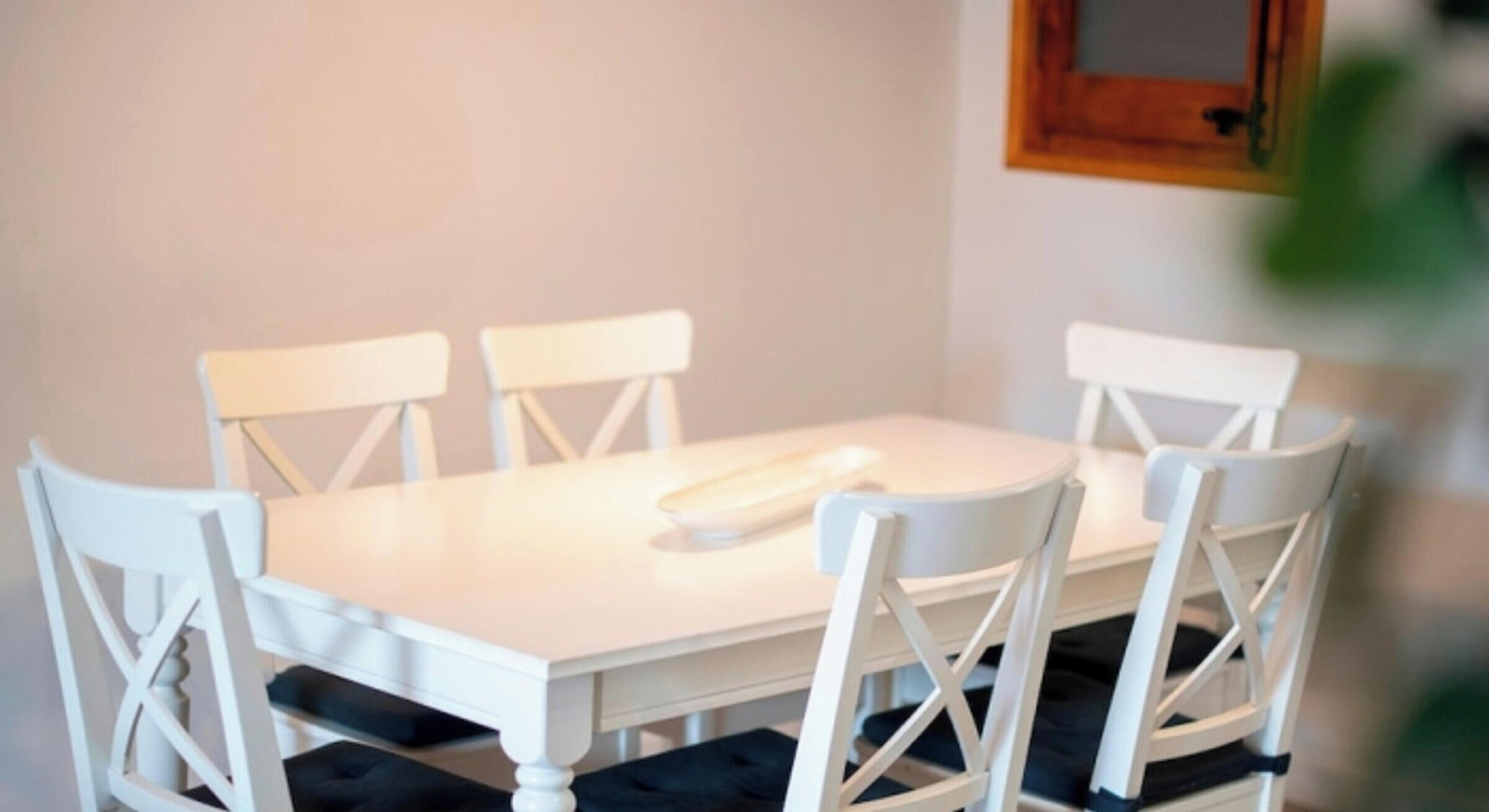 A white dining table with four chairs, each with a black cushion.