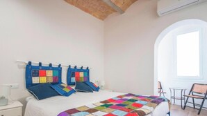 A bedroom with a bed, a nightstand, a lamp, a colorful quilt, and a window with a view. - Modern 2-bedroom apartment in city center, Tarragona (Tarragona)