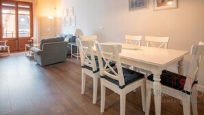 A dining area with a white table and chairs, a grey sofa, and a lamp. There are framed pictures on the wall and a window with curtains. - Modern 2-bedroom apartment in city center, Tarragona (Tarragona)