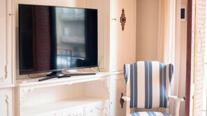 A television on a white cabinet, a striped chair, and a door with a decorative handle. - Modern 2-bedroom apartment in city center, Tarragona (Tarragona)