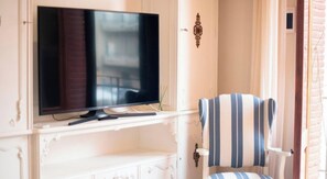 A television on a white cabinet, a striped chair, and a door with a decorative handle. - Modern 2-bedroom apartment in city center, Tarragona (Tarragona)