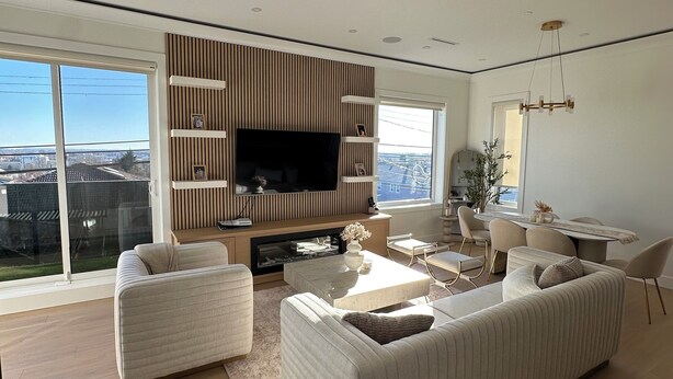 A modern living room with a large TV, wooden panel wall, and a dining area with a table and chairs. - BRAND NEW MODERN 3BR LANEWAY HOUSE (Vancouver)