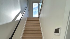 A wooden staircase with a handrail, a door at the top, and a thermostat on the wall. - BRAND NEW MODERN 3BR LANEWAY HOUSE (Vancouver)