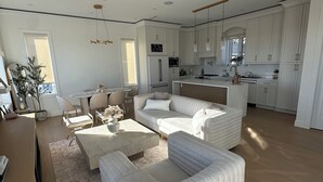 A spacious living room with a large L-shaped sofa, a coffee table, and a dining area with a kitchen in the background. - BRAND NEW MODERN 3BR LANEWAY HOUSE (Vancouver)
