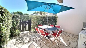 Eine Terrasse mit Tisch, Stühlen, einem blauen Sonnenschirm und einem Grill.