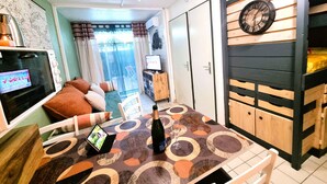 Ein gemütliches Wohnzimmer mit Esstisch, Fernseher und einer Champagnerflasche.