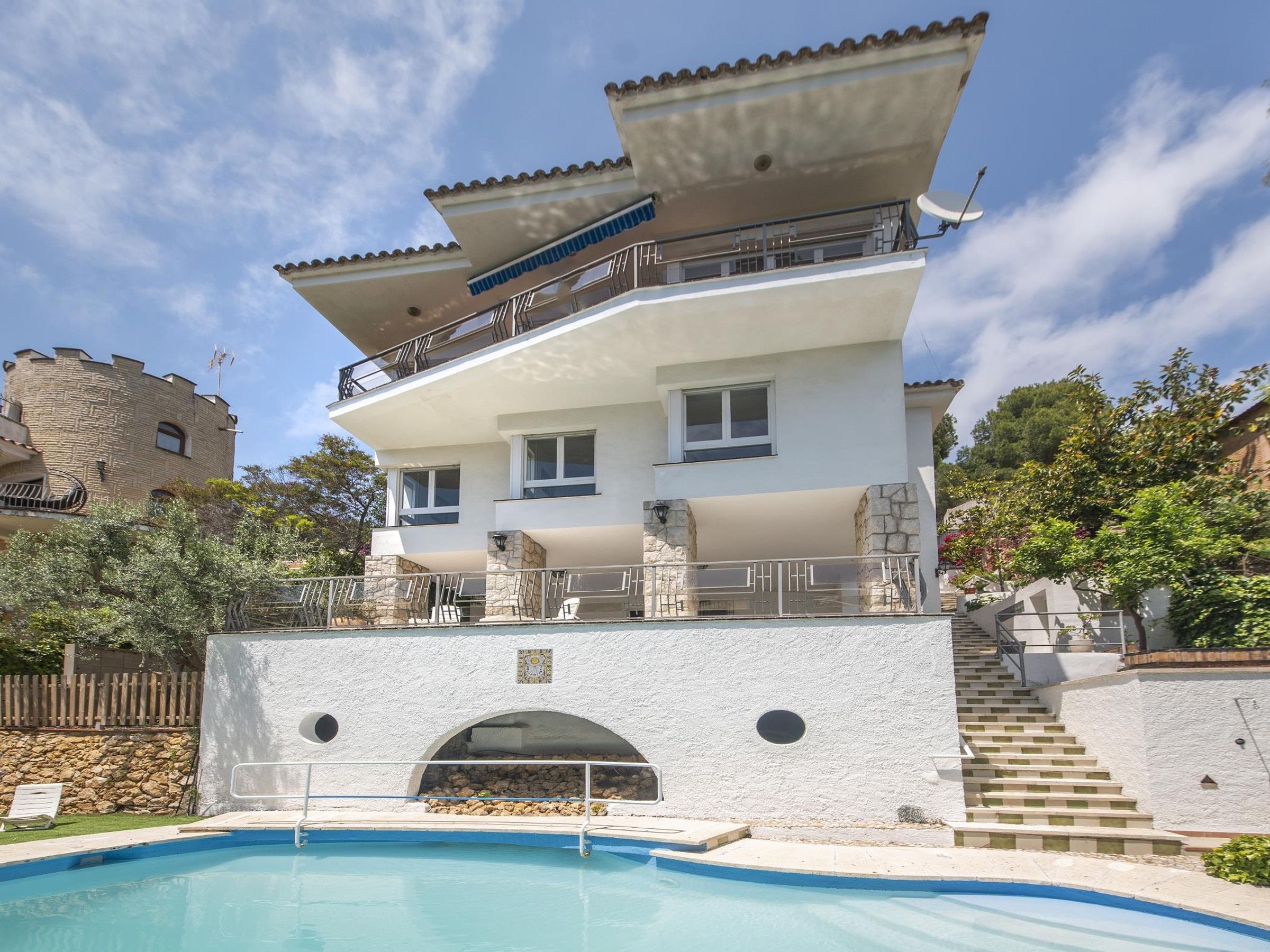 A multi-story building with a swimming pool, balconies, and a stone facade.