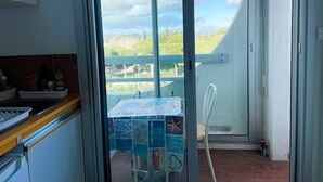 Una cocina con vista a un balcón, una mesa con mantel azul y blanco, y una silla blanca.