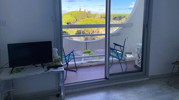 Una habitación con puerta corrediza de vidrio que da a un balcón con vistas a un paisaje verde y un cielo despejado.