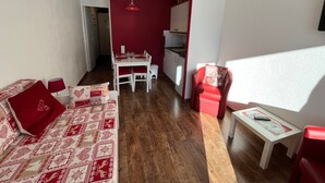 En kompakt opholdsstue med spiseplads, en rød sofa, en rød lænestol og et lille bord.