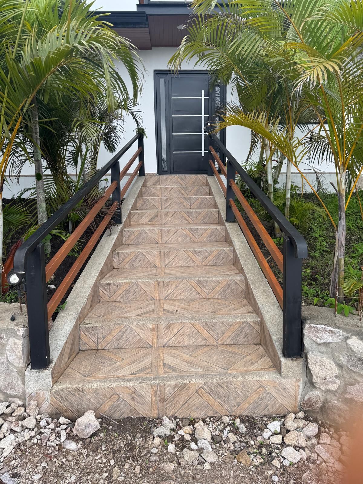 Una escalera con baldosas estampadas, barandillas de metal negro y palmeras.