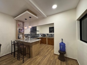 A modern kitchen with a central island, bar stools, a water dispenser, and pendant lighting. - Modern Country House with Heated Pool in Yunguilla Valley Near Cuenca Ecuador (Santa Isabel)