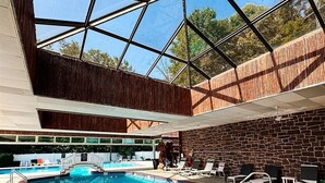 An indoor swimming pool with a glass ceiling, a brick wall, and lounge chairs.