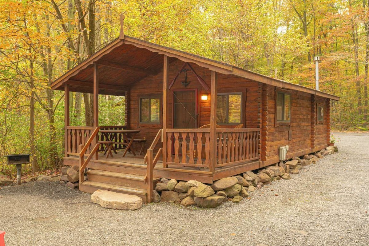 A wooden cabin with a porch, steps, and a gravel driveway.