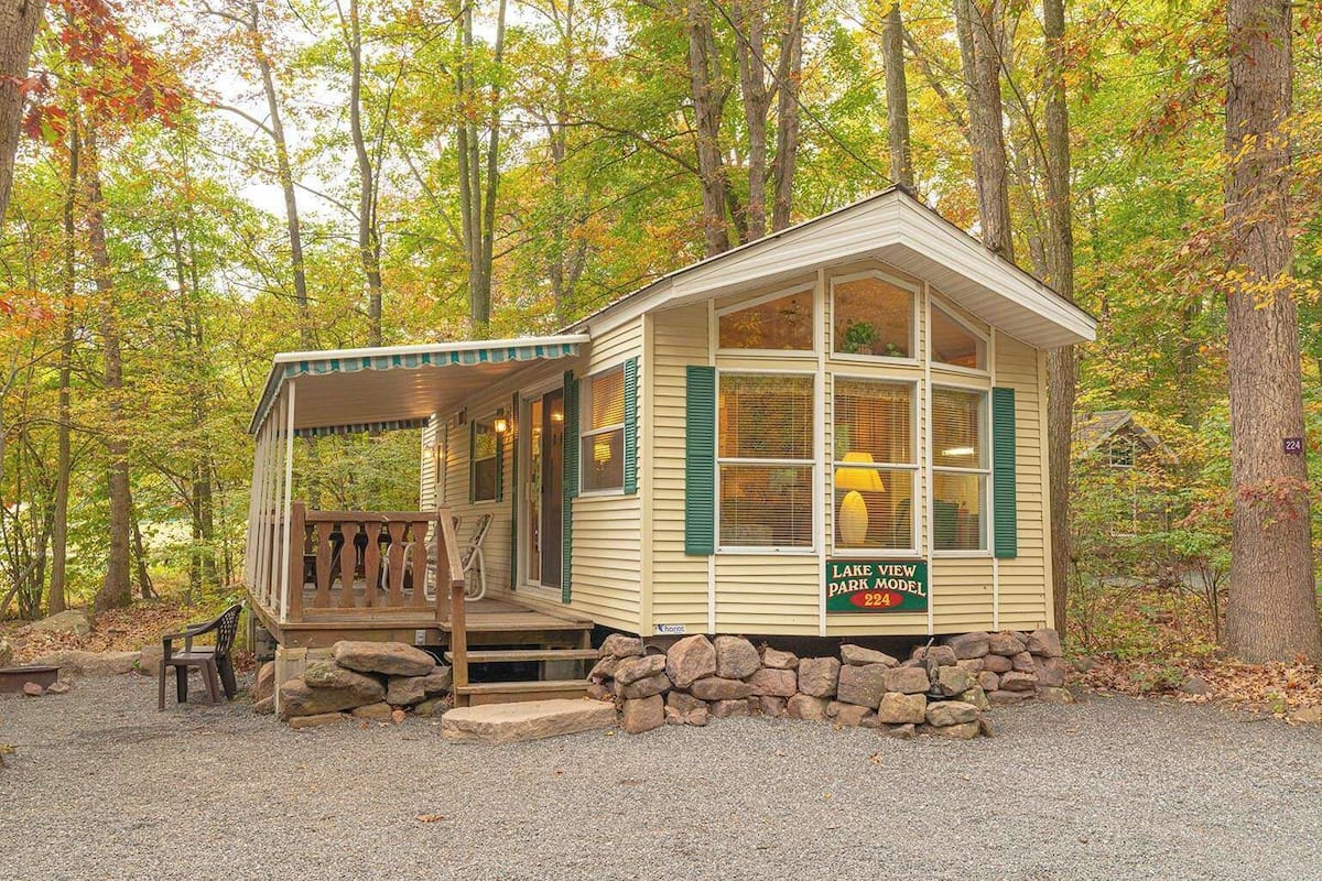 A cabin with a porch, a sign reading 'Lake View Park Model 224,' and a stone foundation.