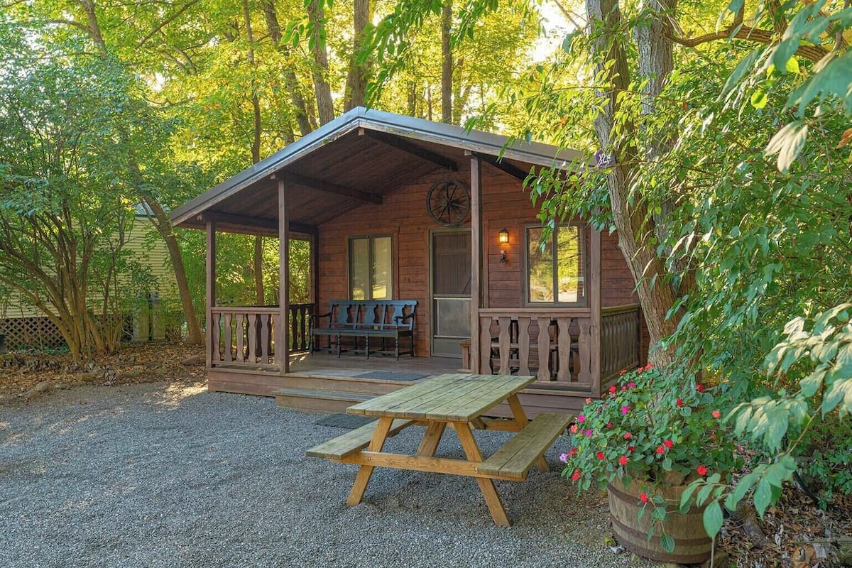 A rustic cabin with a porch, a bench, and a picnic table.